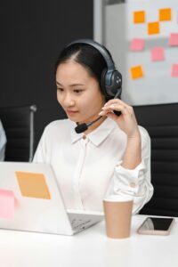Asian woman using a laptop and headset for customer support in an office environment.