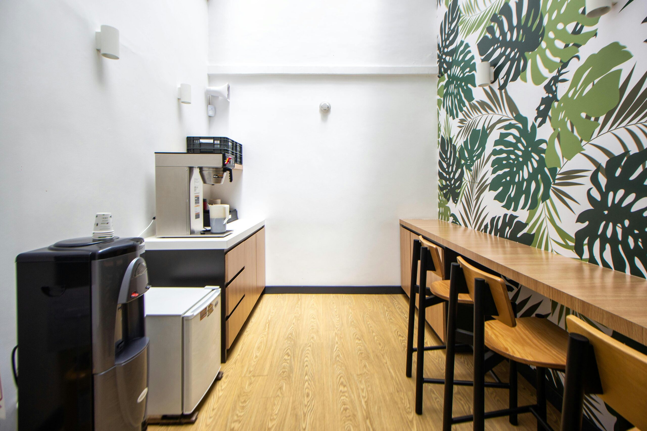 Bright kitchenette area with coffee machines and botanical wallpaper for a refreshing break.